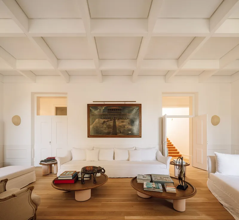 White coffered ceiling above a salon with timber floors and symmetrical doorways flanking a framed painting