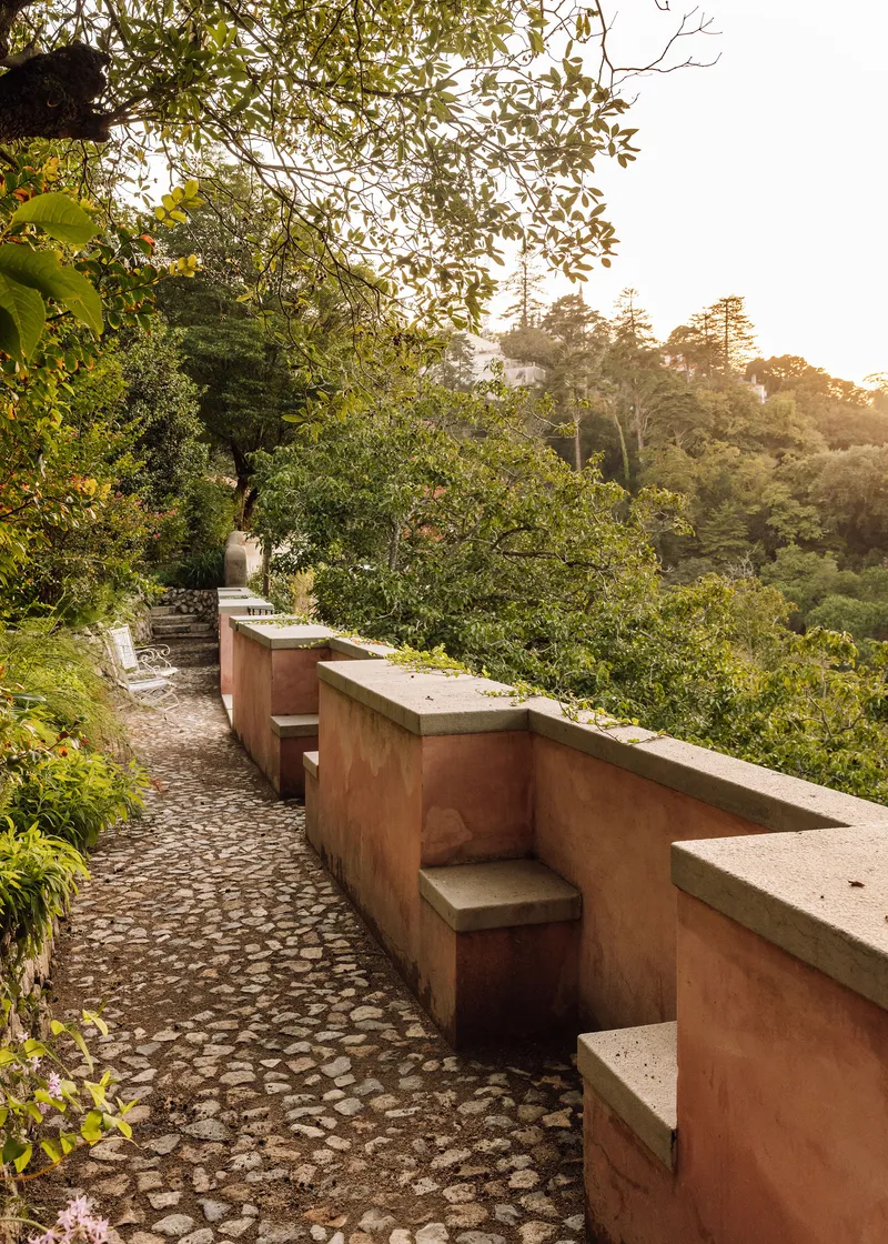 Cobblestone terrace with integrated concrete bench seating along a planted hillside in late afternoon light