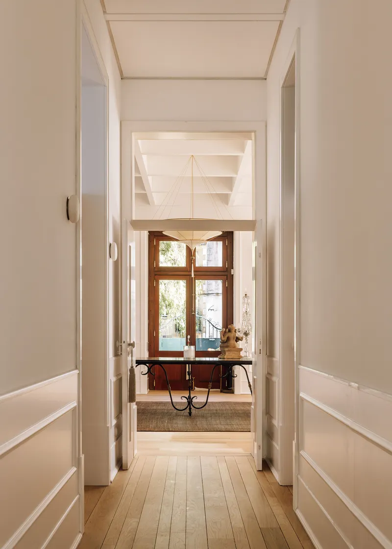 Axial view through white paneled hallway toward timber console table beneath a window with daylight