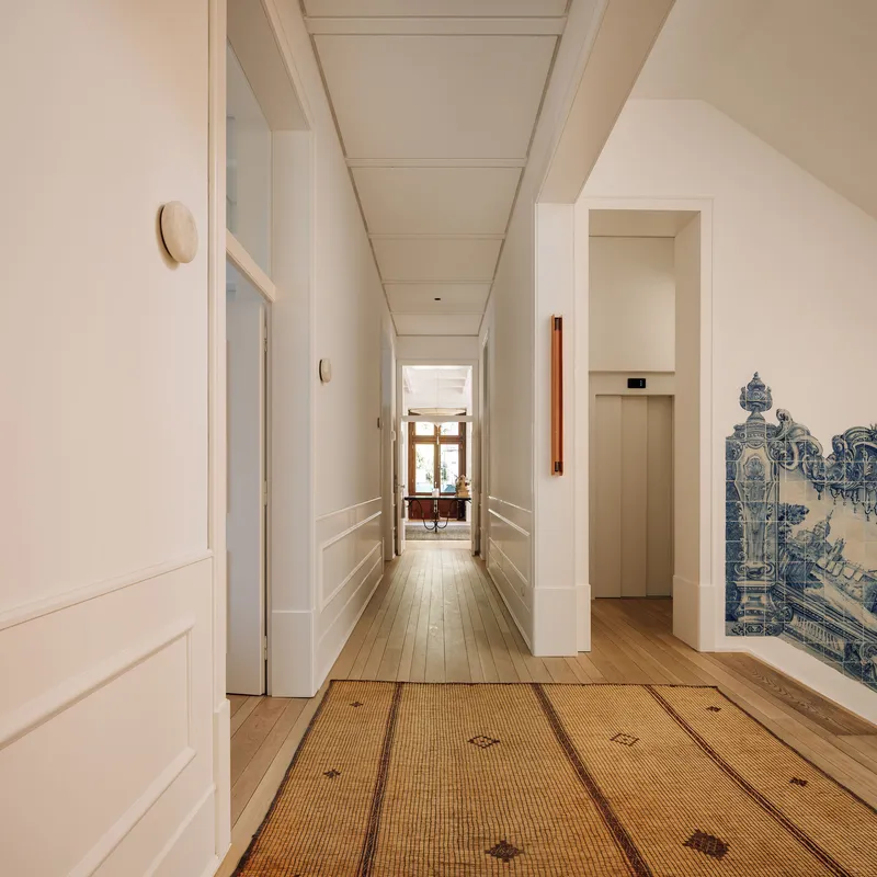 White corridor with patterned carpet runner, coffered ceiling, and blue tile panel at corridor terminus