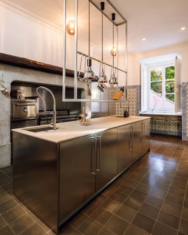 Kitchen island with brushed steel cabinetry and suspended pulley pendant lights under warm artificial light