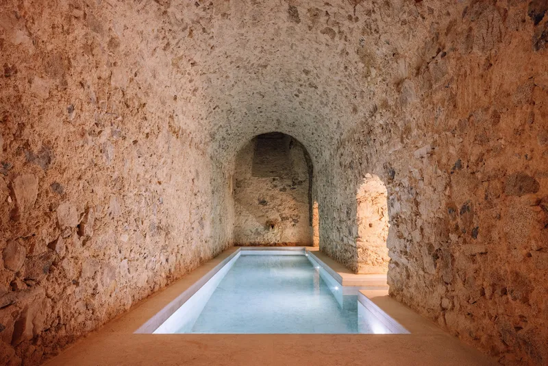 Rectangular plunge pool set in a vaulted stone grotto with arched niche and warm timber flooring