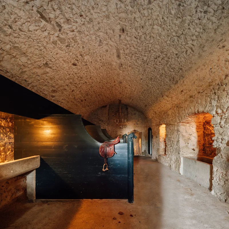 Vaulted corridor with exposed stone walls and ceiling lit by recessed amber lighting