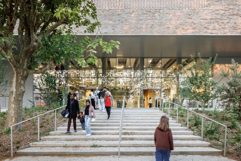 Wide entry staircase leading to the glazed lobby with visitors ascending between planted beds