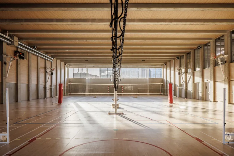 Sports hall with exposed timber beam ceiling and volleyball nets suspended over the court