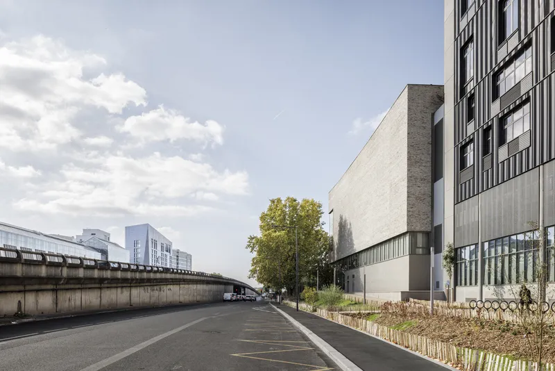 Street view showing the textured facade volume beside an elevated roadway under scattered clouds