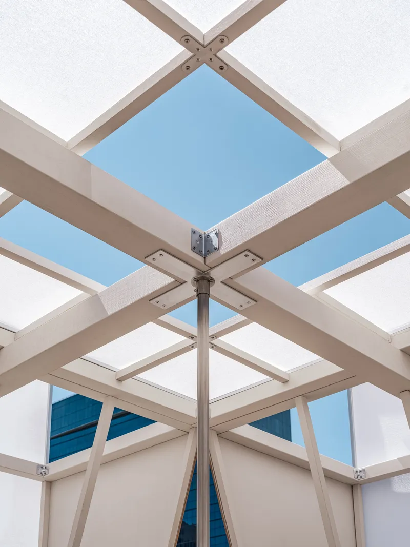 Upward view of the pavilion's central steel column connecting timber beams and translucent roof panels