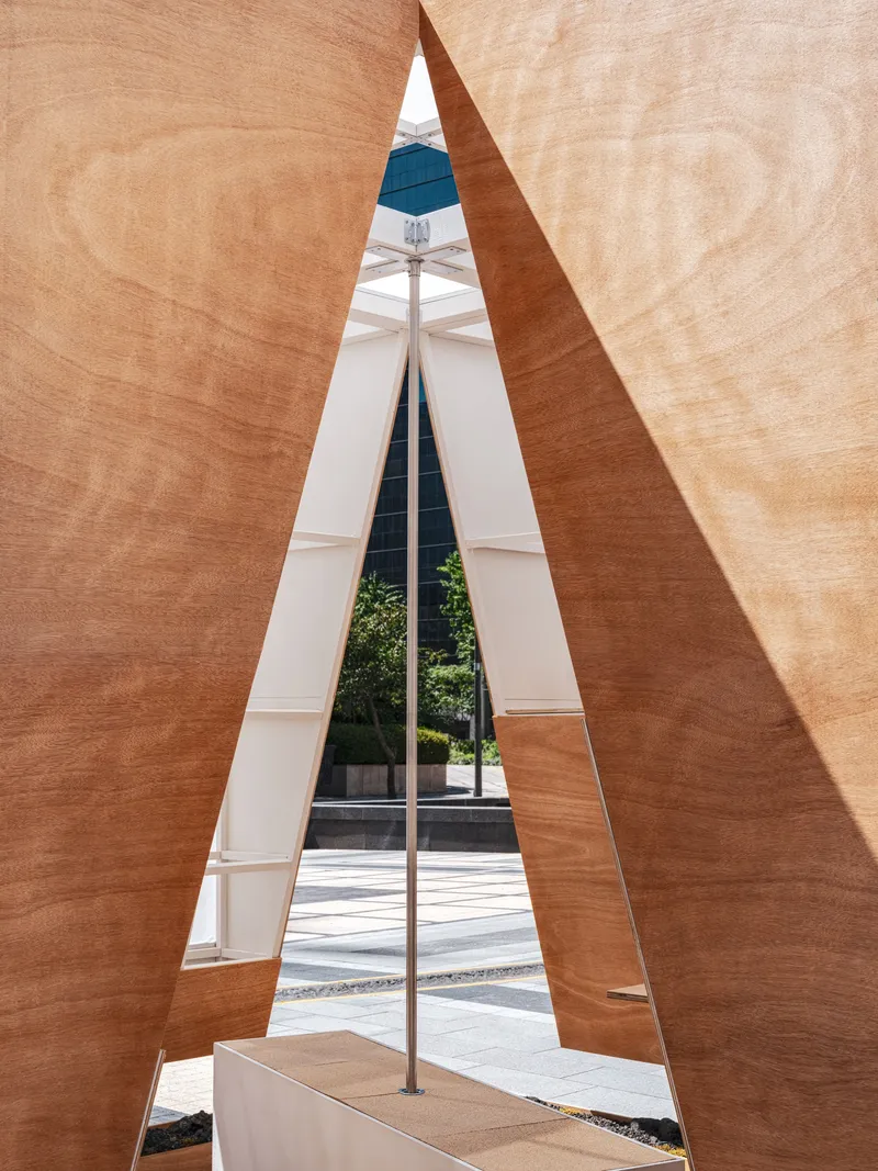 View through narrow triangular opening formed by converging plywood walls revealing the street beyond