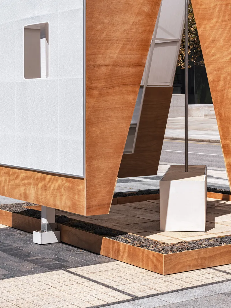 Ground-level detail of laminated timber panels on white metal posts with a black aggregate base