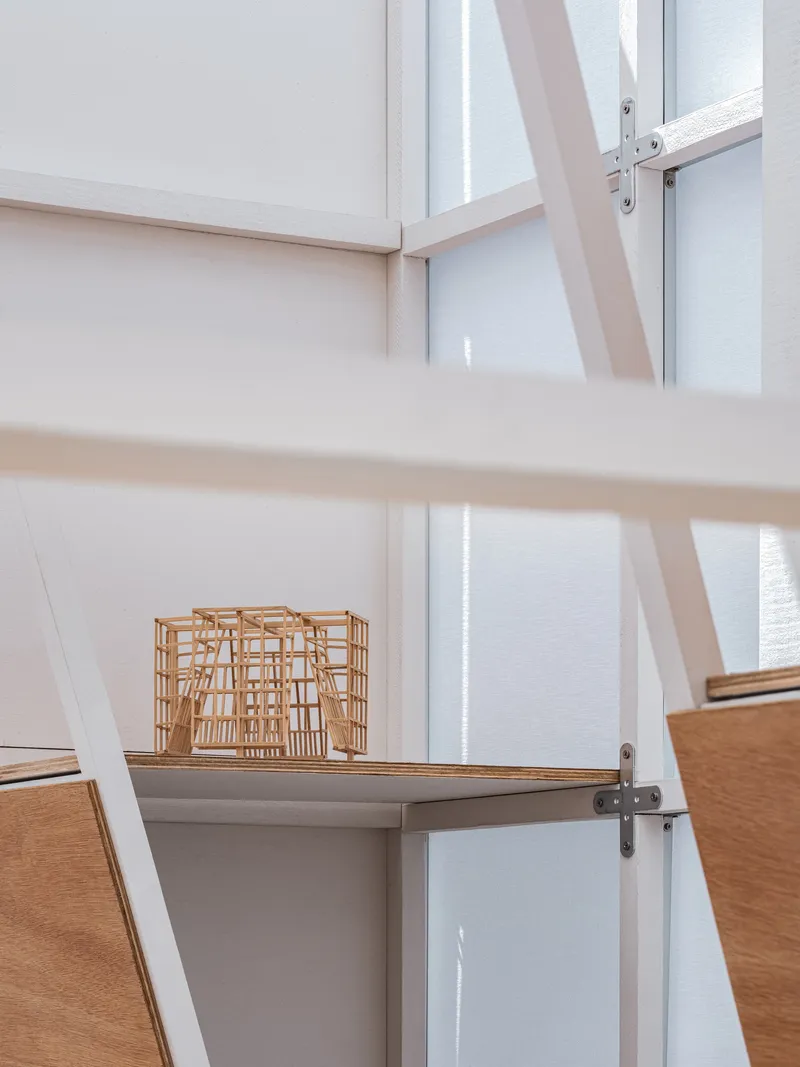 Interior display shelf with white framework and a small architectural model in soft daylight