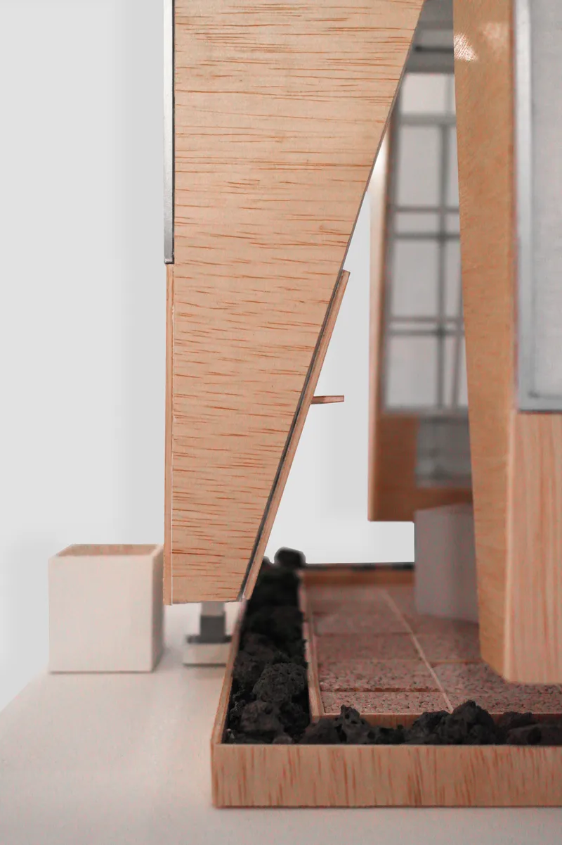 Close-up of a model's angled timber facade panel with black gravel plinth