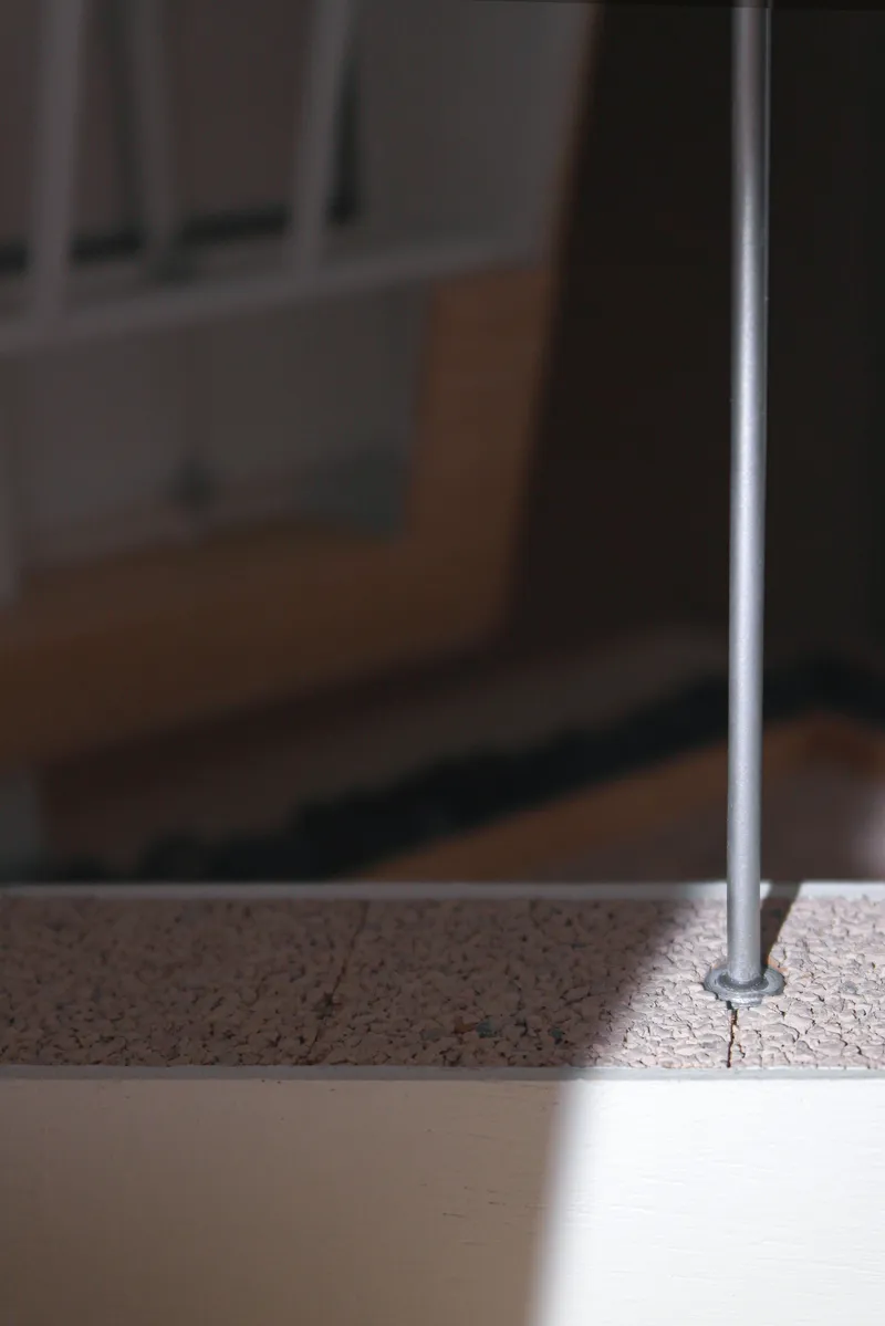 Detail of a slender steel rod anchored into a speckled terrazzo floor