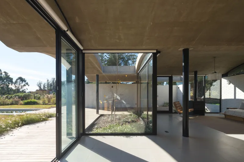 Interior view through pivoting glass doors toward a central courtyard with a single planted tree