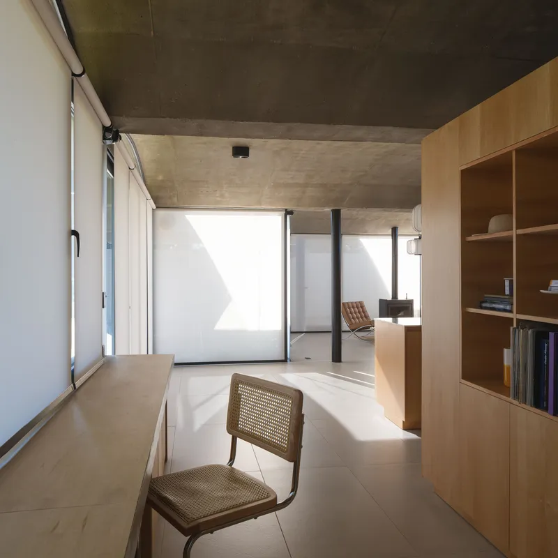 Interior corridor with exposed concrete ceiling and light wood joinery illuminated by afternoon sun