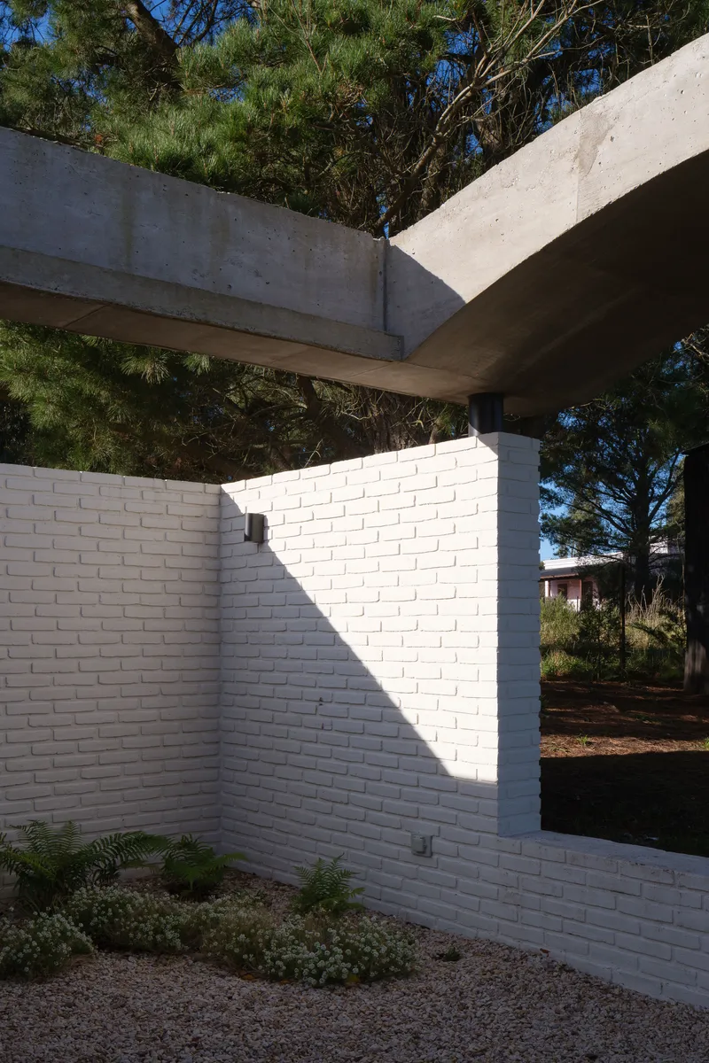 White brick courtyard wall meeting concrete roof beams amid eucalyptus trees