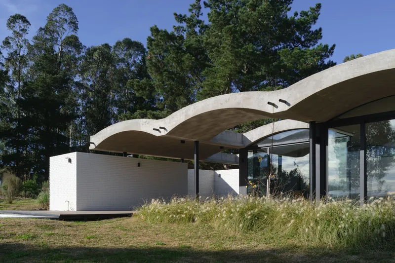 Side elevation showing the scalloped concrete canopy floating above white brick walls and glazed openings in bright daylight