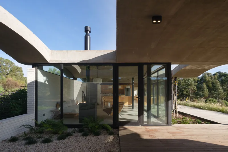 Exterior corner with glazed walls beneath overlapping concrete roof shells and a metal flue pipe rising above
