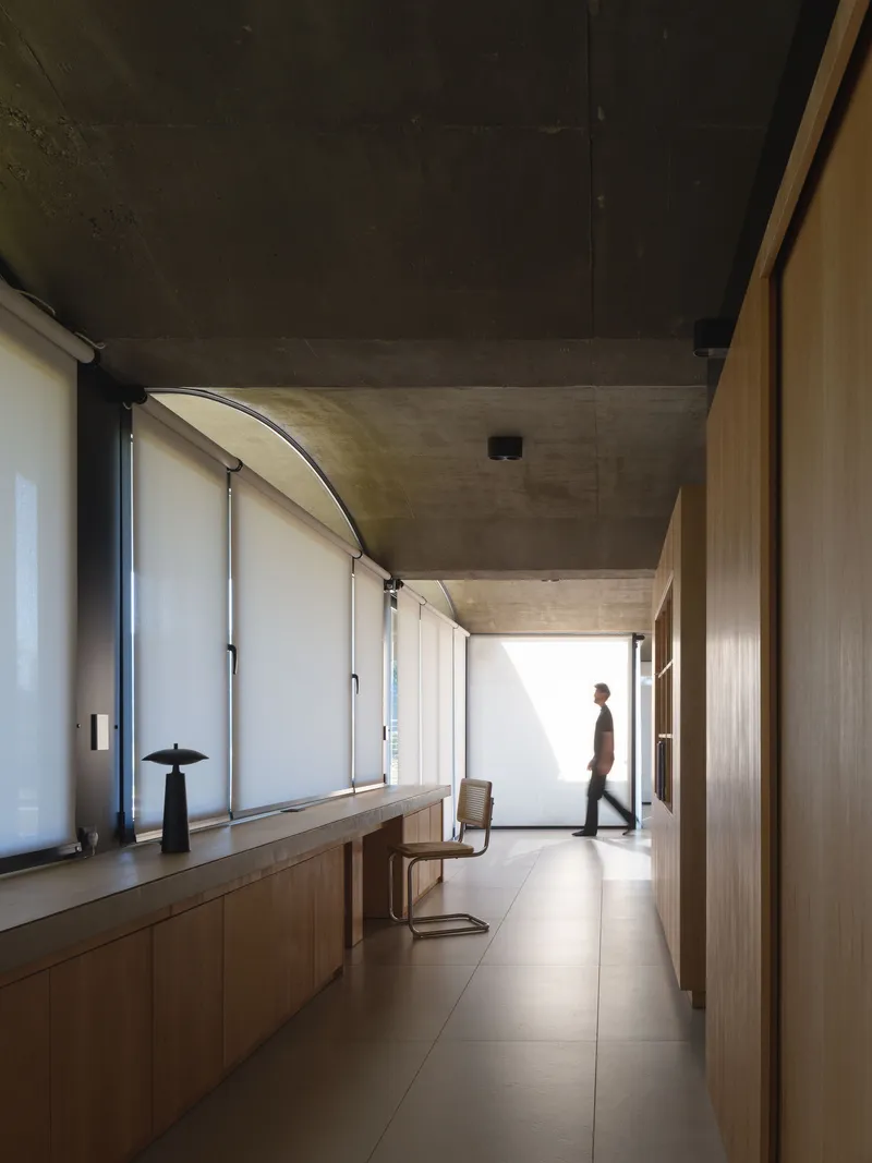 Interior corridor with timber cabinetry along one wall and a figure walking toward light at the far end