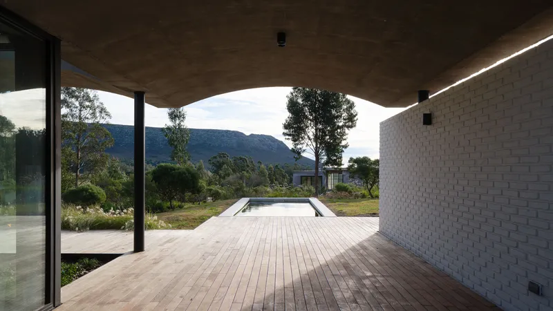 Covered deck overlooking a rectangular pool and mountain range under an arched concrete soffit
