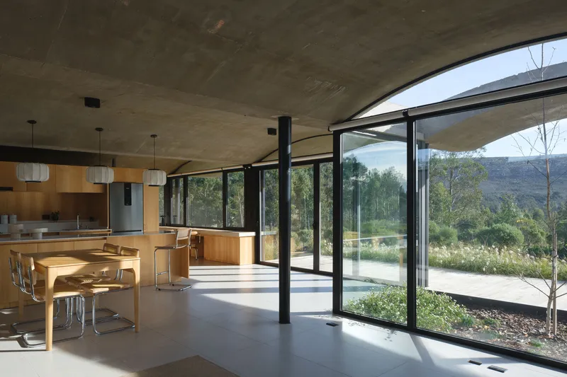 Open-plan kitchen and dining area with curved concrete ceiling and floor-to-ceiling glazing
