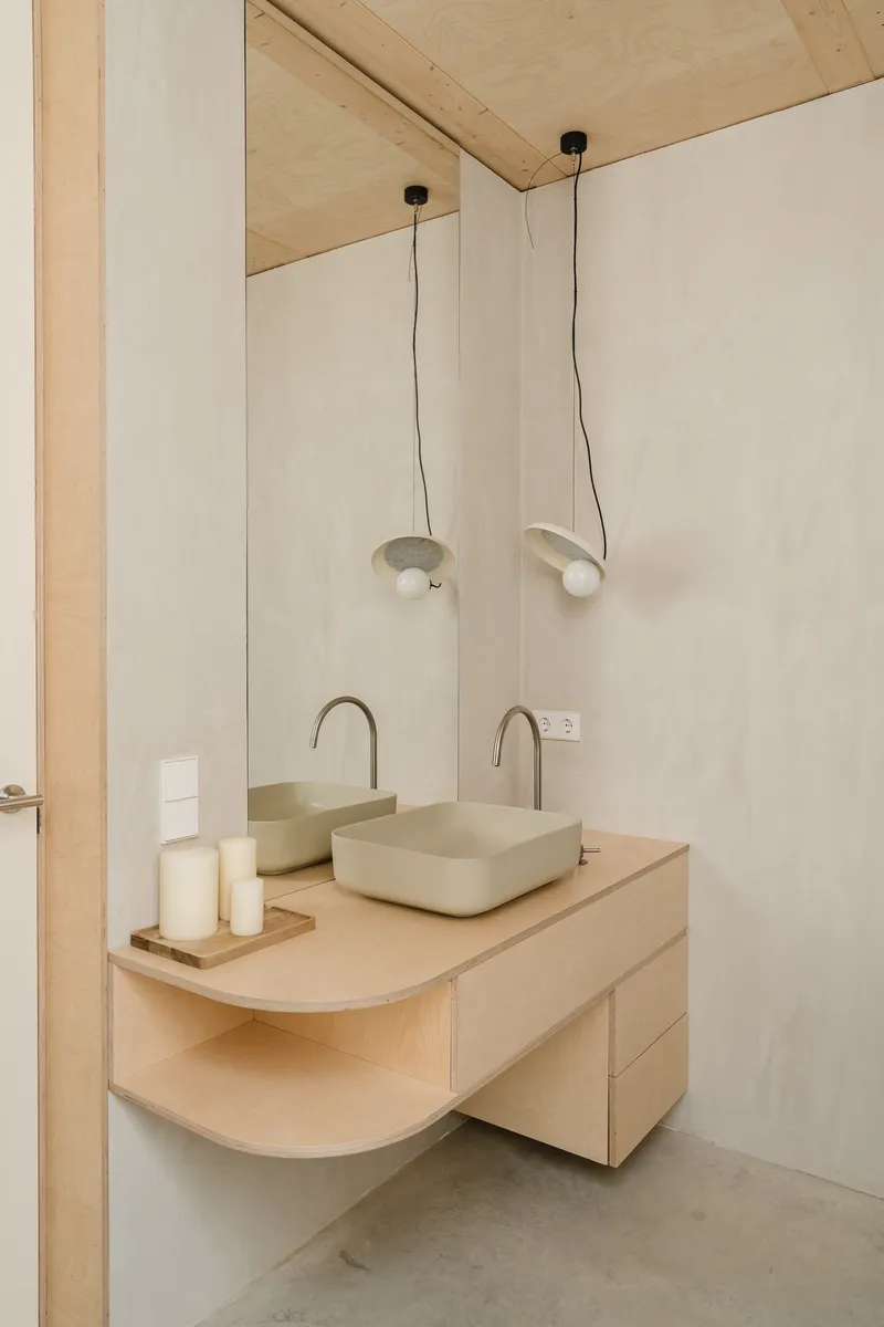 Bathroom vanity with twin vessel sinks, curved plywood counter and pendant lights hanging from the exposed plywood ceiling