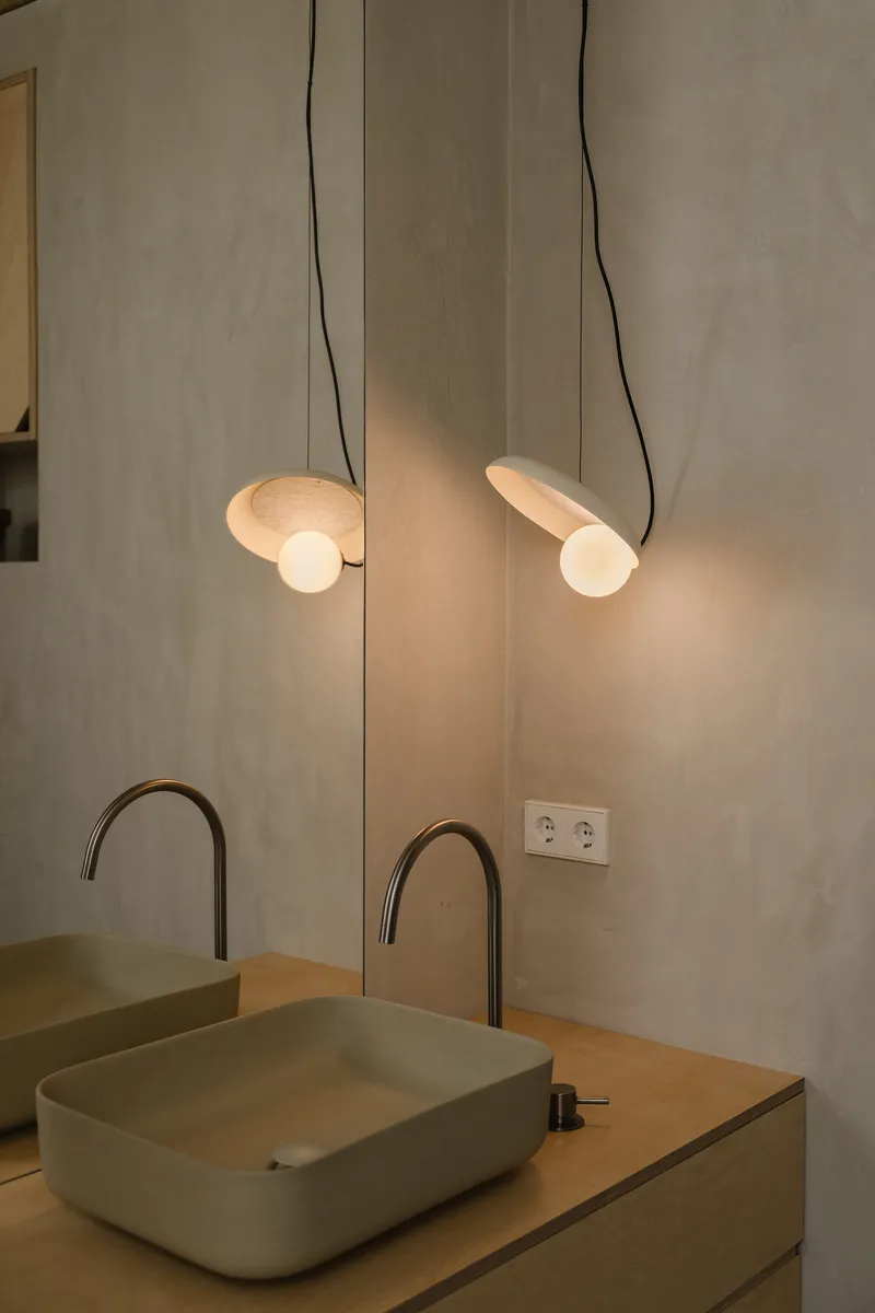 Close-up of the illuminated pendant lights suspended above pale green vessel sinks with arched faucets
