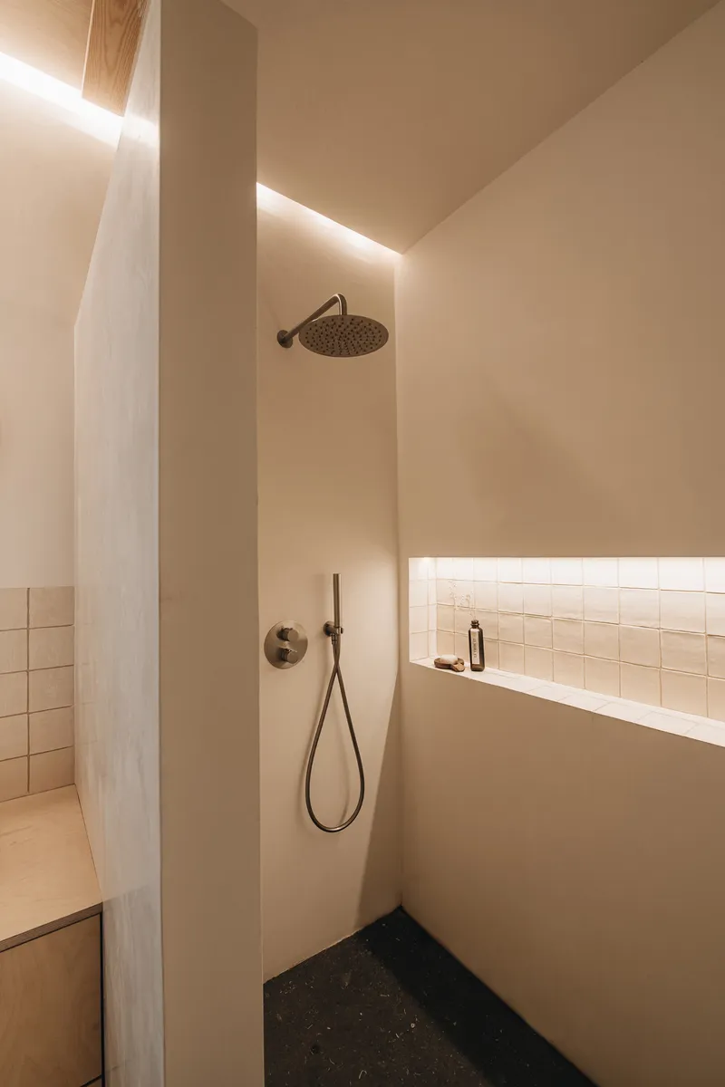 Shower corner with overhead rain fixture, polished plaster walls and concealed linear lighting at the ceiling