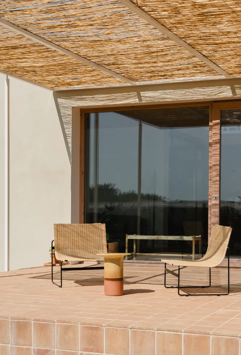 Terrace with woven rattan chairs beneath a bamboo slat pergola and full-height glazed doors