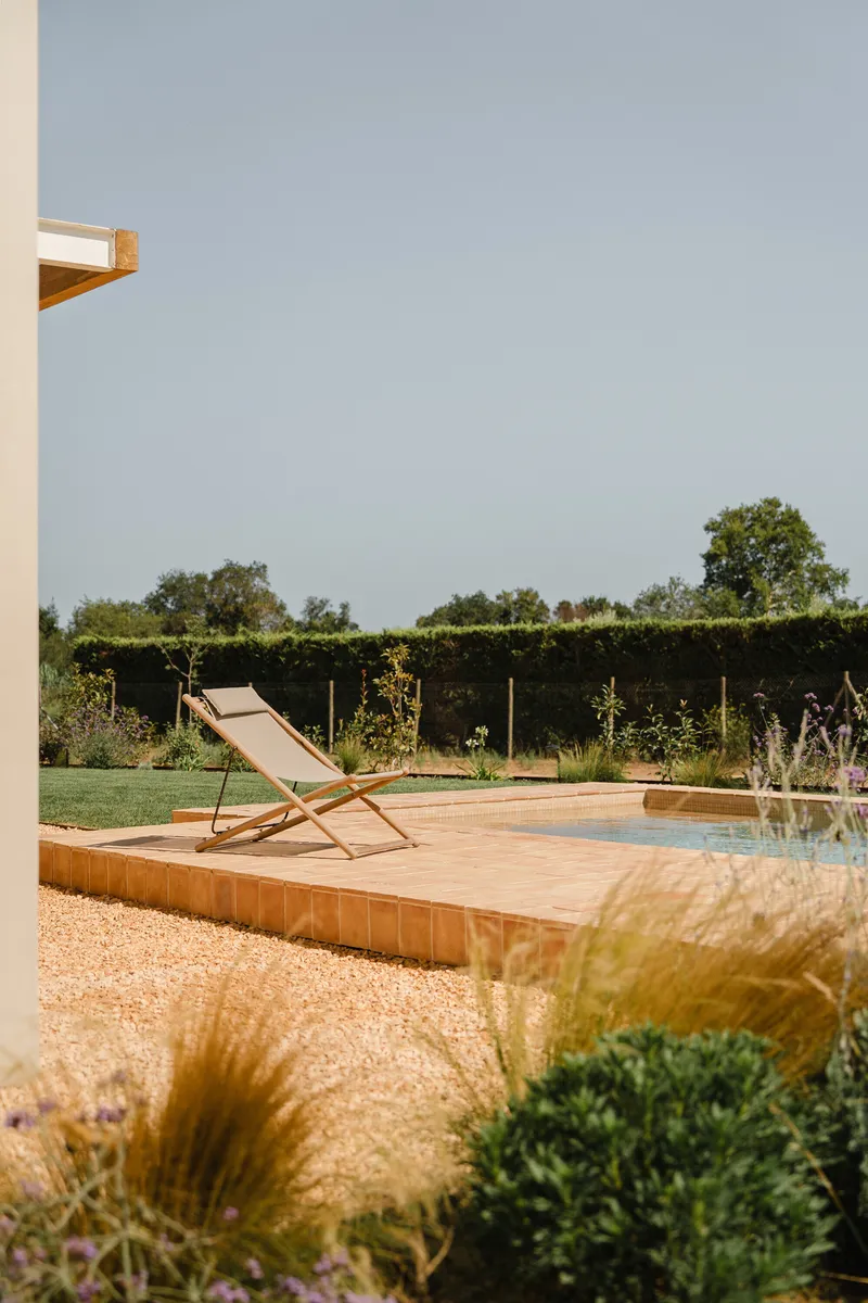 Timber deck terrace with canvas lounge chair beside gravel garden and hedgerow