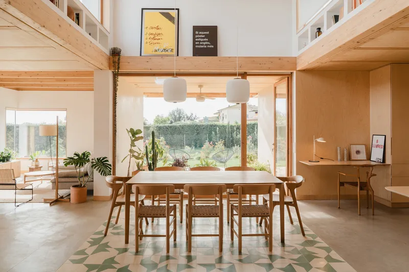 Dining table on geometric tile rug beneath structural timber frame and pendant lights