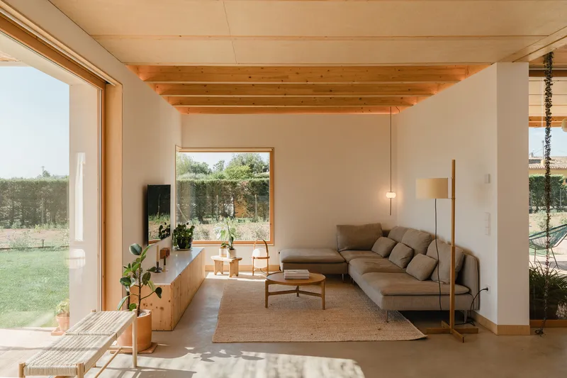Living room with exposed timber ceiling beams and large window framing views of the grassy lawn beyond