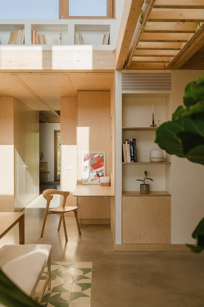 Dining area with plywood cabinetry and upper mezzanine visible through open timber stair treads above