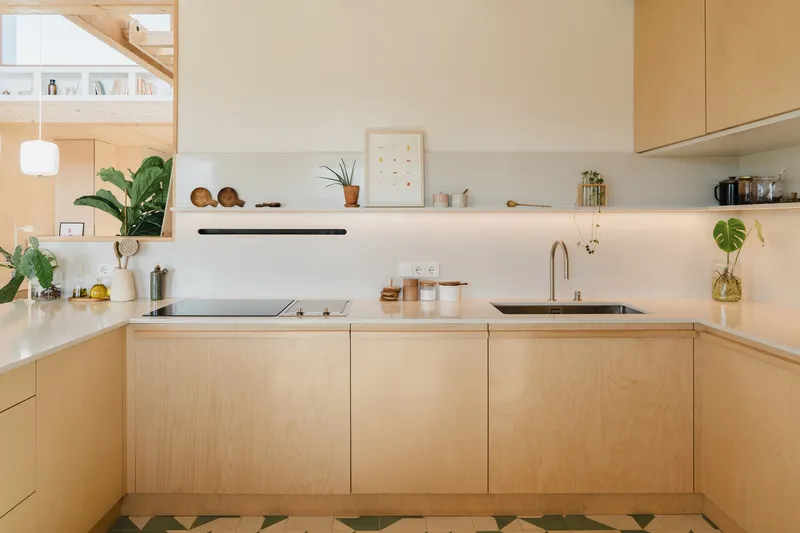 Corner kitchen with pale wood cabinetry and geometric floor tiles meeting polished concrete flooring