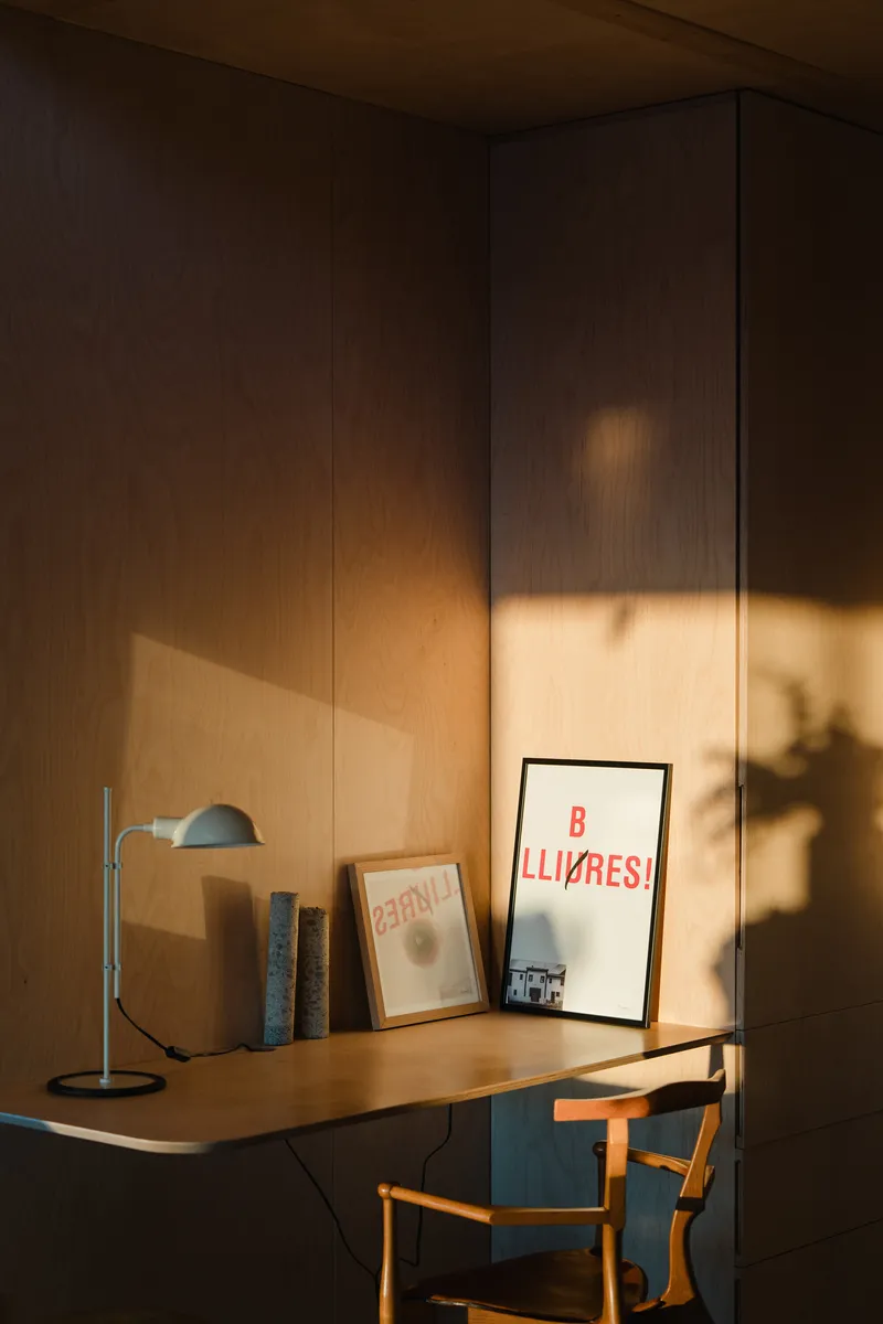 Plywood desk alcove with framed prints and desk lamp illuminated by golden evening light