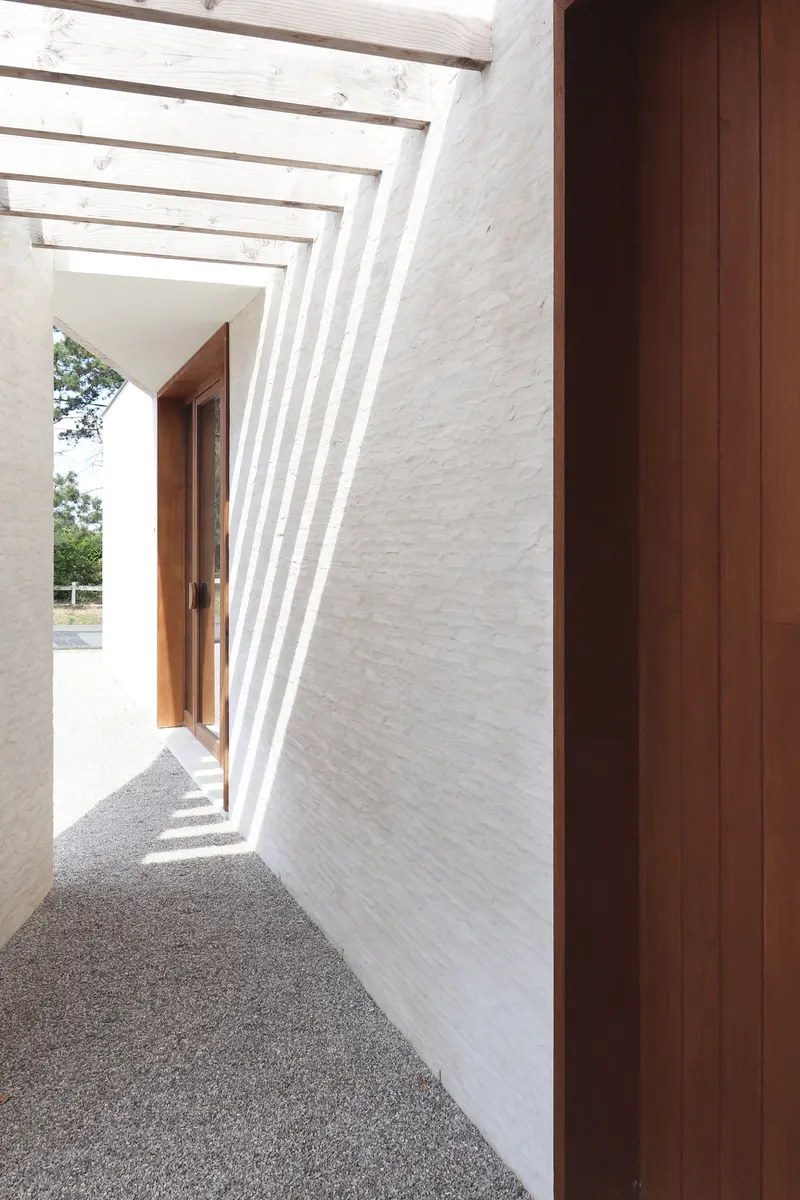 View through the angled concrete ribs of the entry canopy casting shadows on the white brick wall