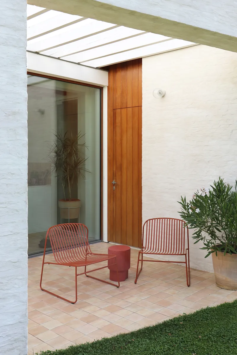 Covered terrace with timber door, glass wall, terracotta tile floor and red metal chairs