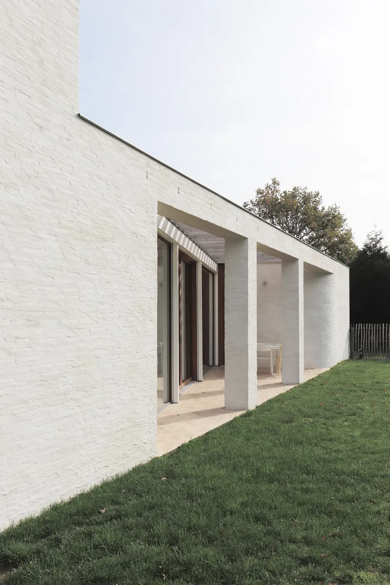 Recessed porch with concrete columns and deep overhang set into white brick facade