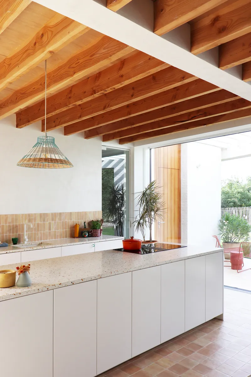 Kitchen island with terrazzo countertop and white cabinetry beneath exposed timber joists and recessed lighting