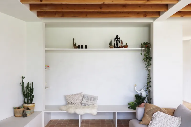 Built-in white bench with open shelving above and timber ceiling beams, flanked by potted cacti and plants