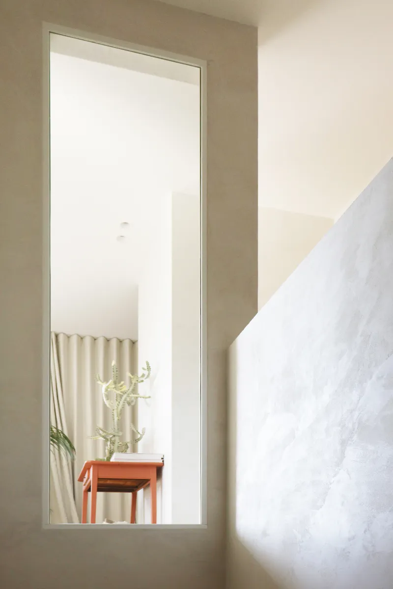Tall narrow window framing a view of a console table with cactus and wall hangings beyond
