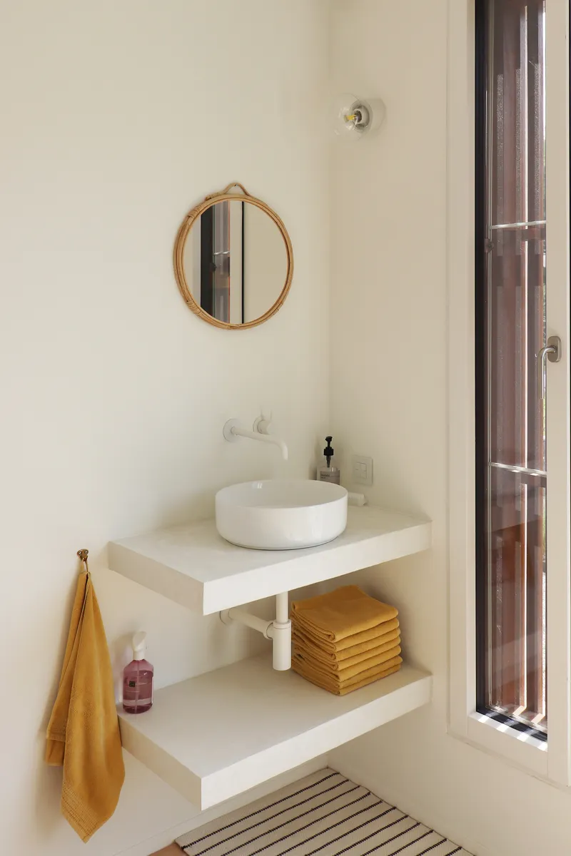 Bathroom vanity with floating shelves, round vessel sink, circular mirror and tall louvered wooden door