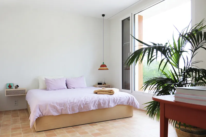 Bedroom with terra-cotta tile floor and full-height glazing framed by potted palm fronds
