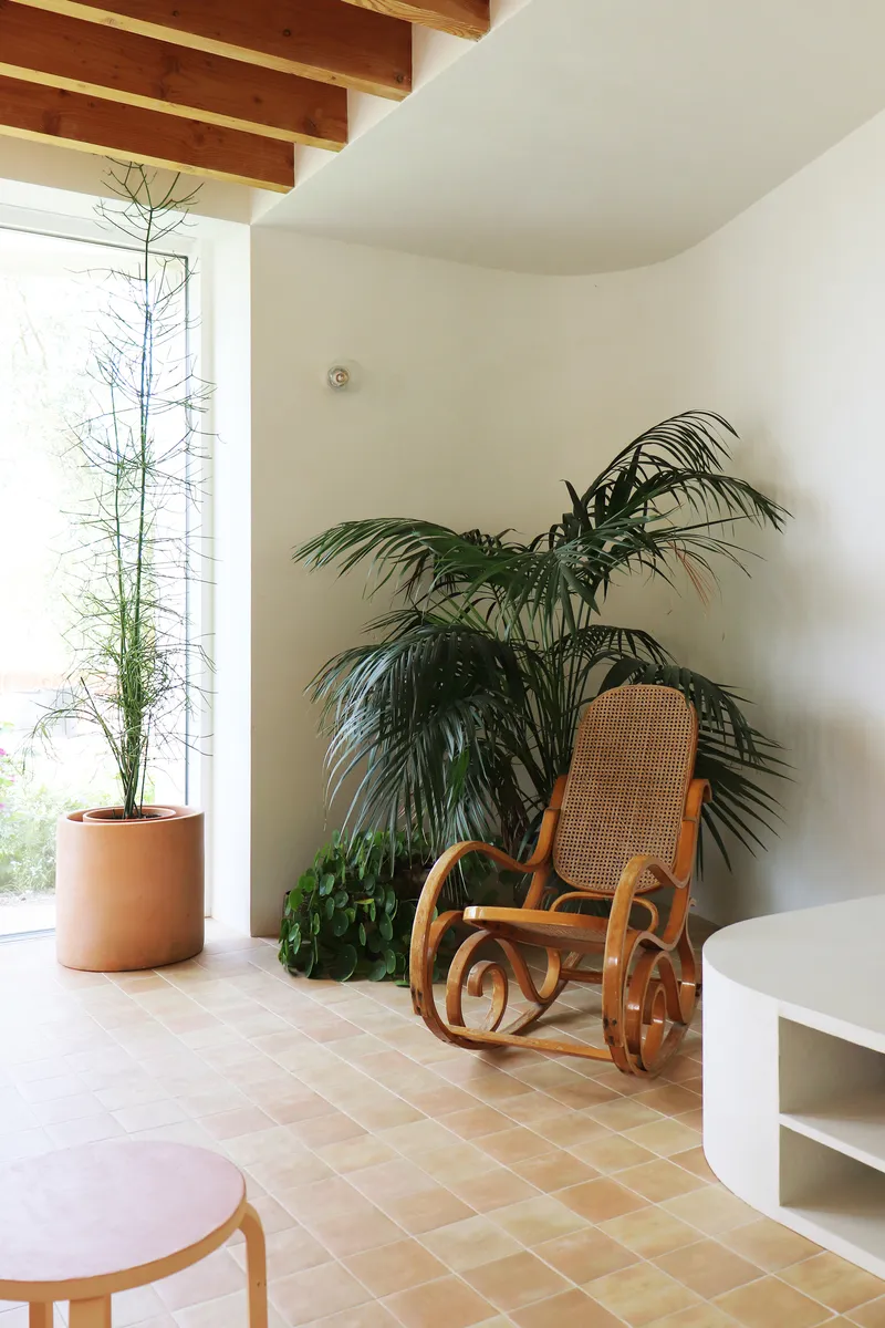Living area corner with bentwood rocking chair beside potted palms and exposed timber beams overhead