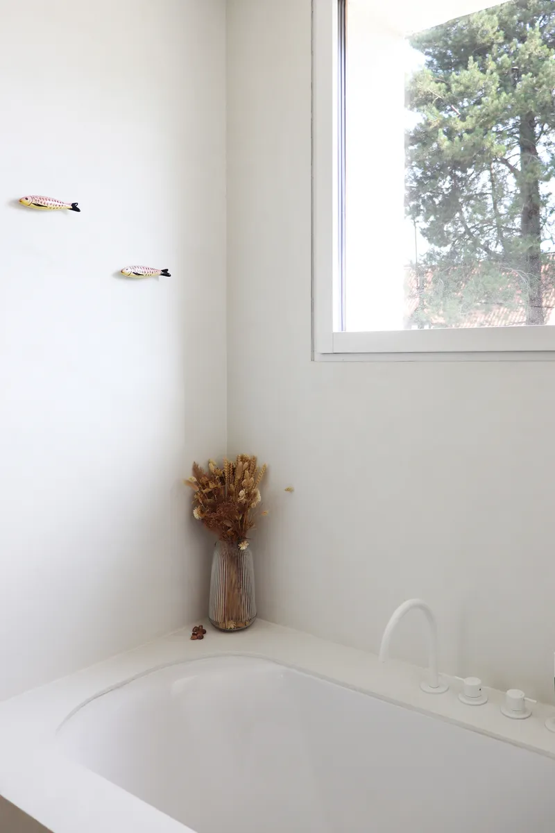 Bathtub corner with dried floral arrangement under a window overlooking mature trees
