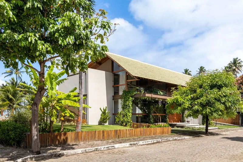 Street view of the gabled tile roof rising above a vertical timber fence and tropical planting
