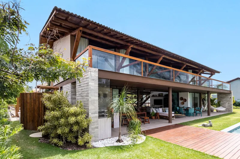 Two-story residence with exposed timber structure, terracotta tile roof and planted beds with palms in foreground