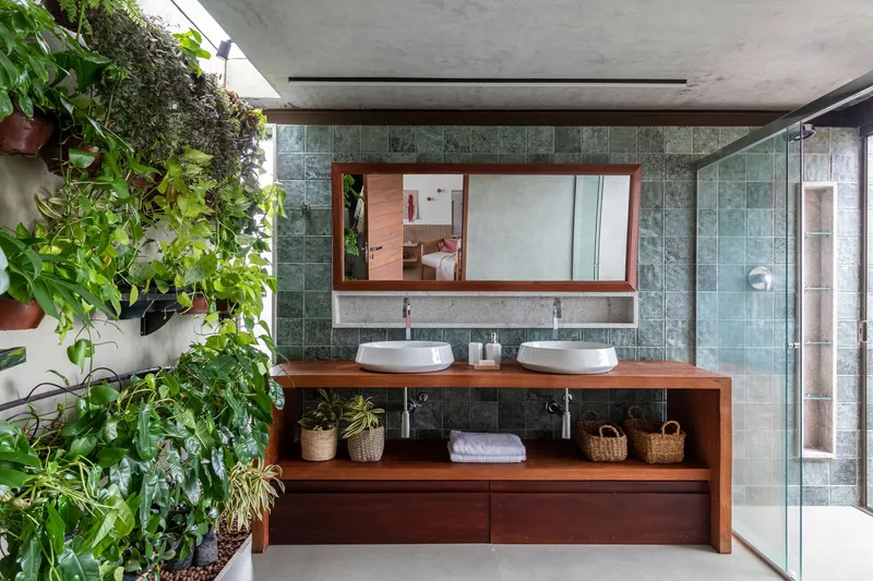 Bathroom vanity with twin white basins on timber counter beneath green stone tile wall and vertical garden