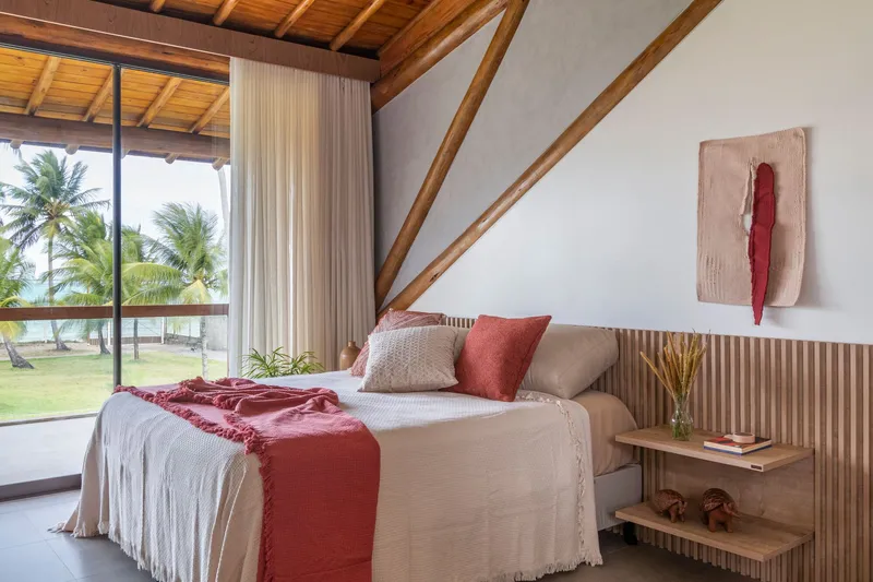 Bedroom with glazed doors opening to palm trees and fluted timber headboard beneath exposed rafters
