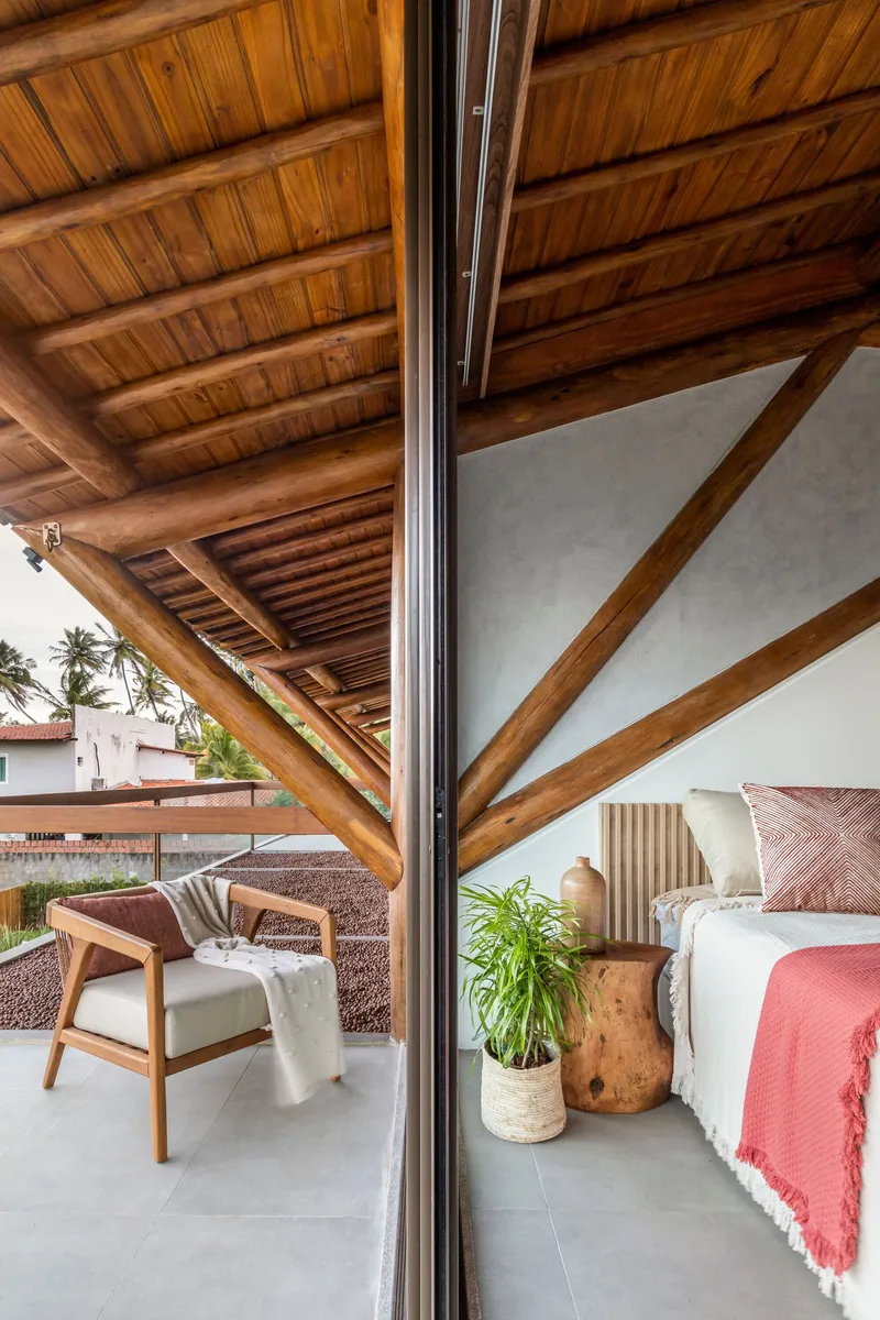 Glass partition separating bedroom from covered terrace beneath exposed timber beam ceiling structure