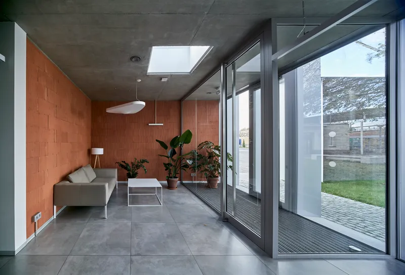Interior lobby with vertical terracotta tile wall and glazed doors opening to a courtyard